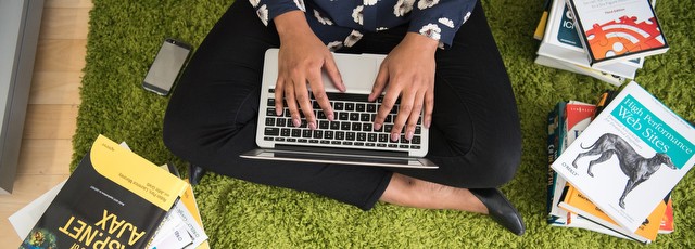 Person sitting cross-legged, working on a laptop, surrounded by books