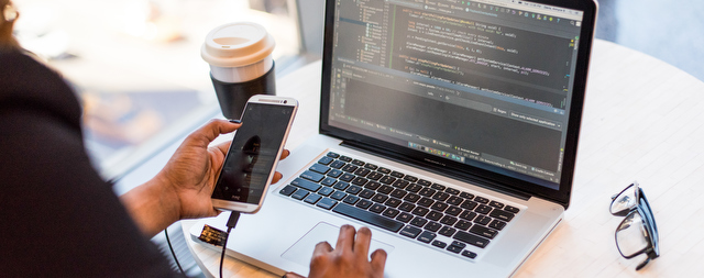 A person at their laptop with a phone and coffee in-hand